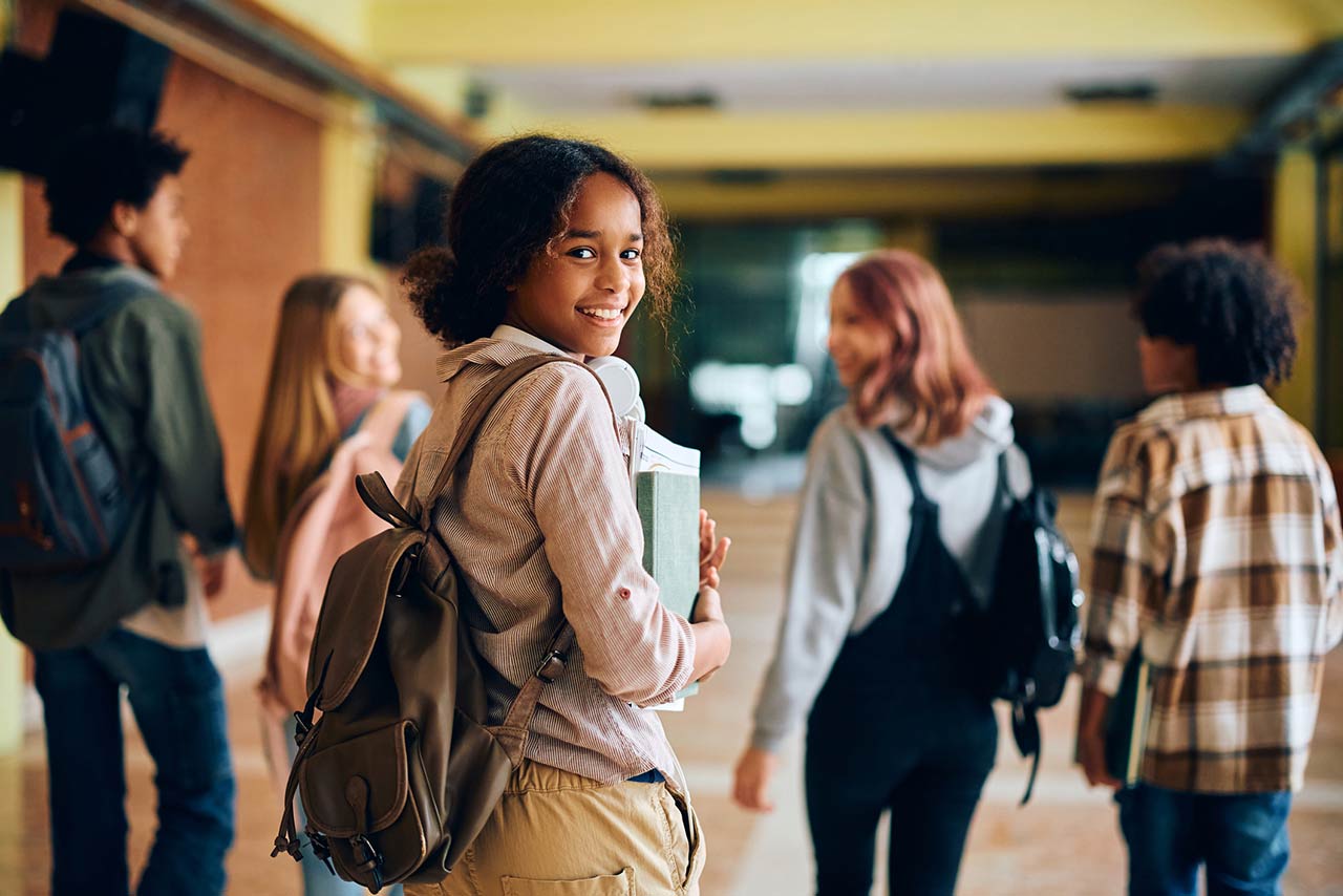 Happy African American high school student walking through hallway with her friends and looking at camera